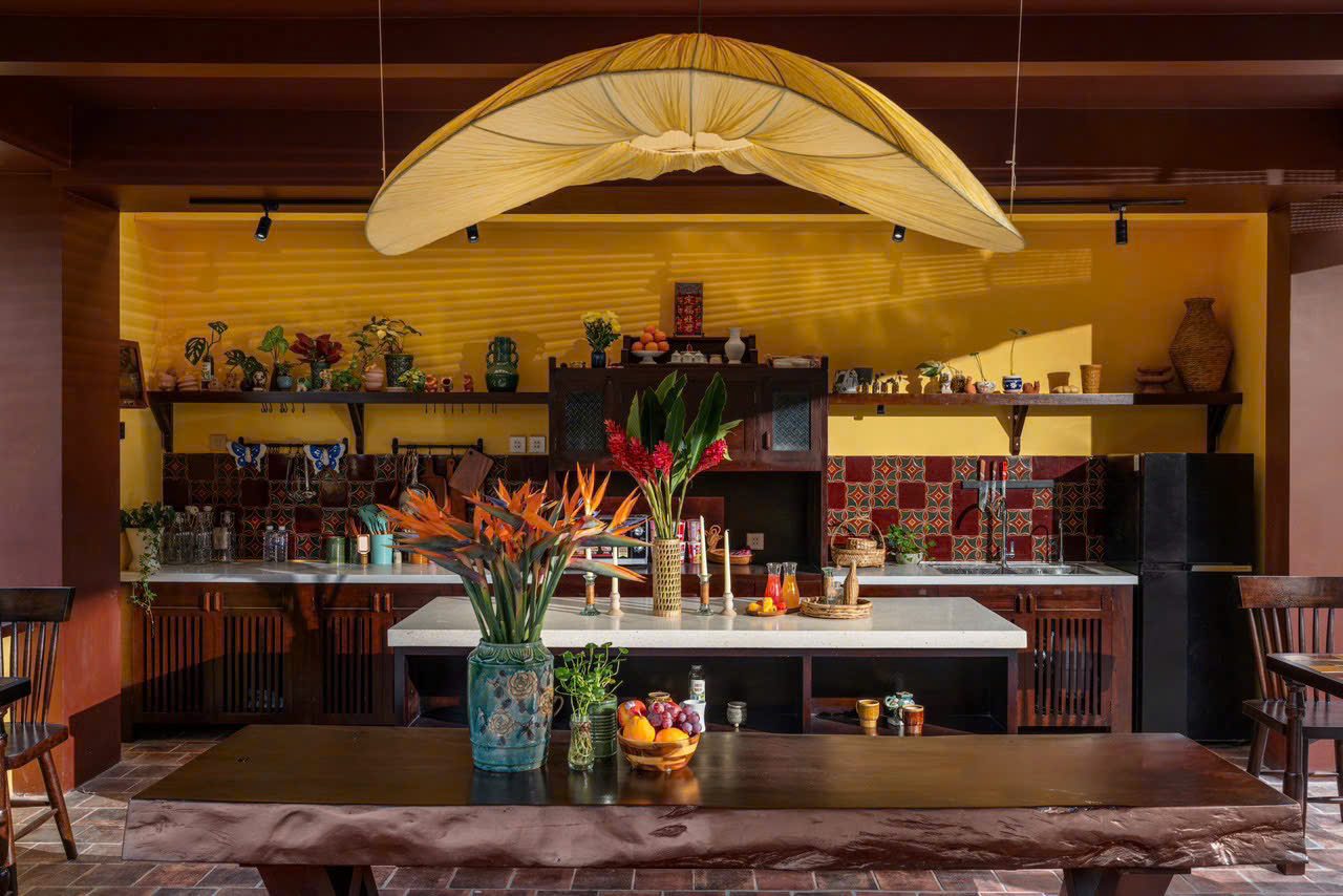 Open kitchen with mustard walls, a long wooden table and a large paper lamp