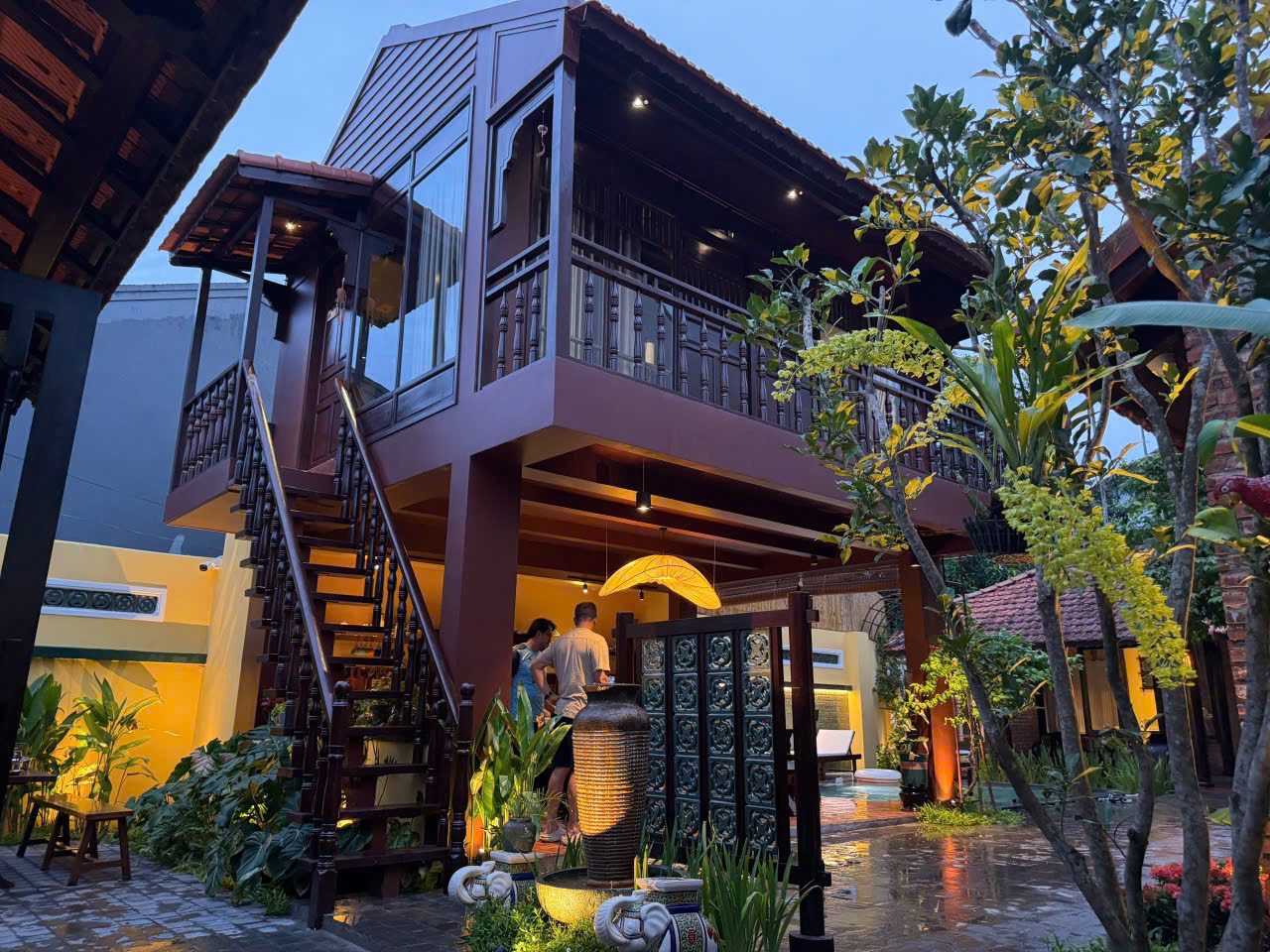 Two-storey wooden stilt house lit up at night among garden plants