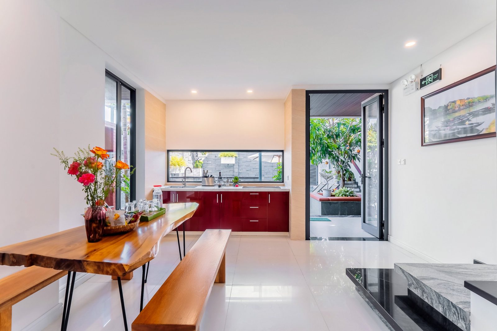Red kitchen cabinets and a live-edge wooden dining table by glass doors