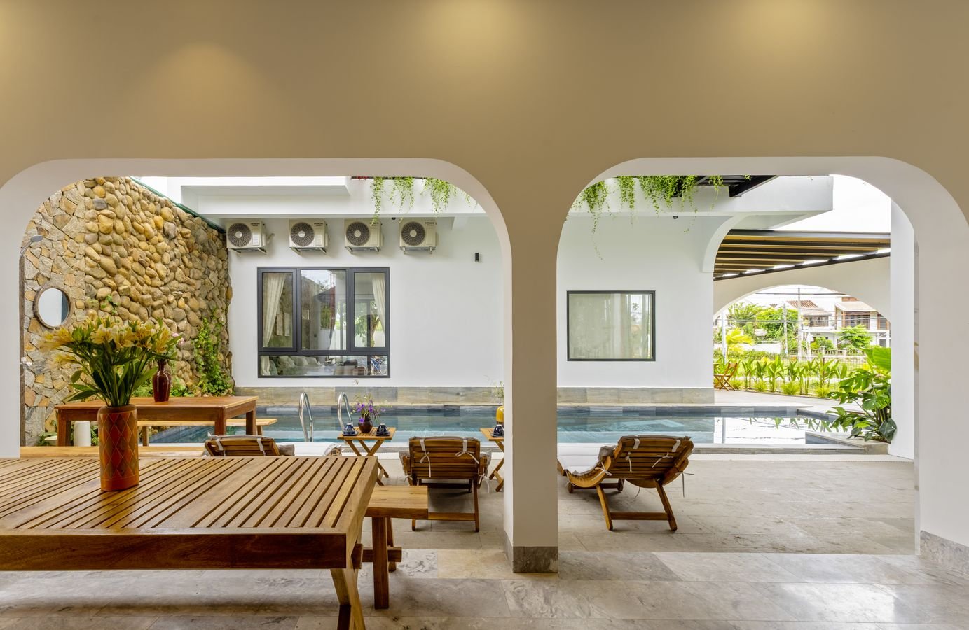 Arched terrace with a wooden dining table looking onto the pool