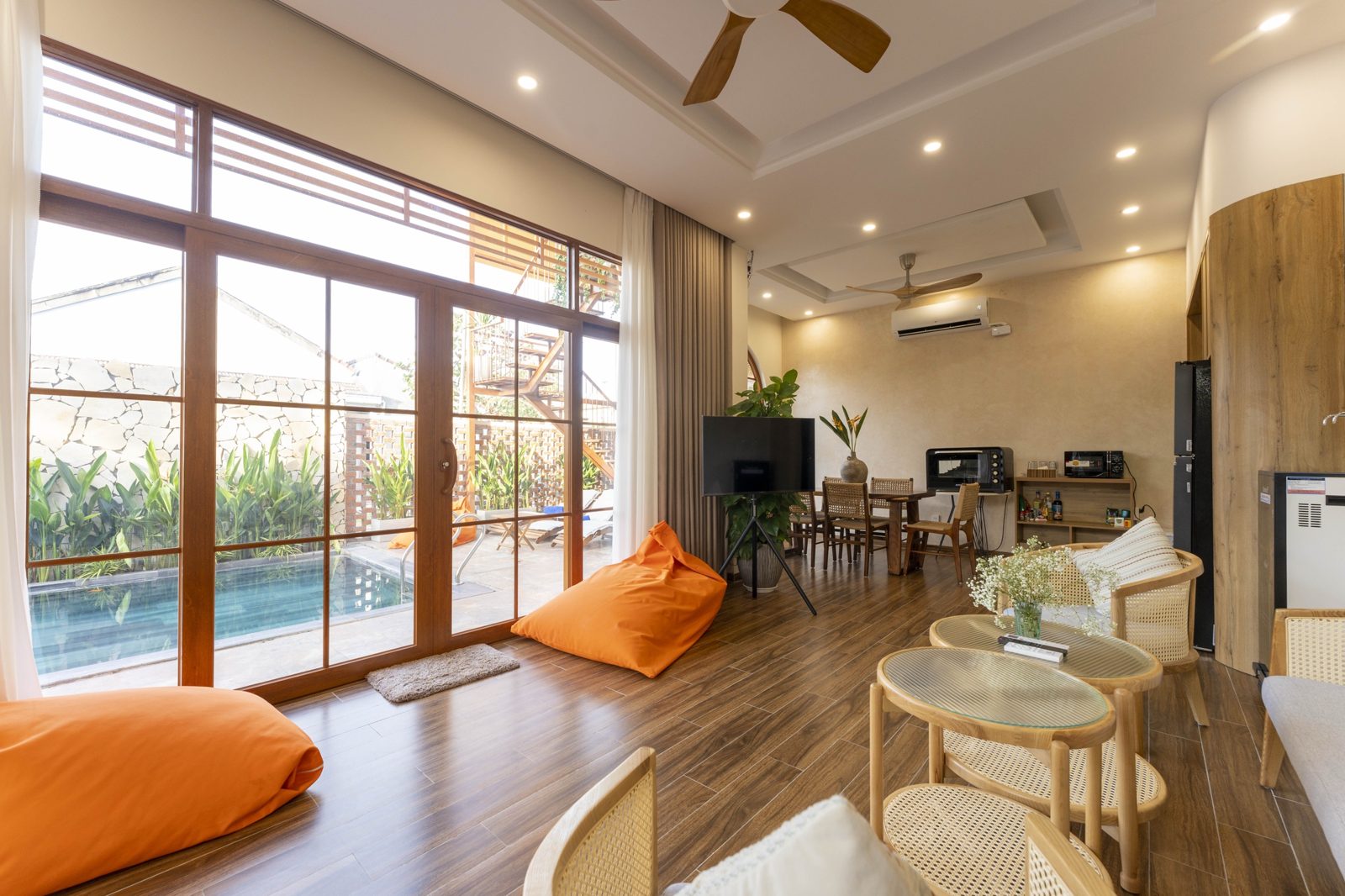 Living room with orange bean bags and tall glass doors opening onto the pool