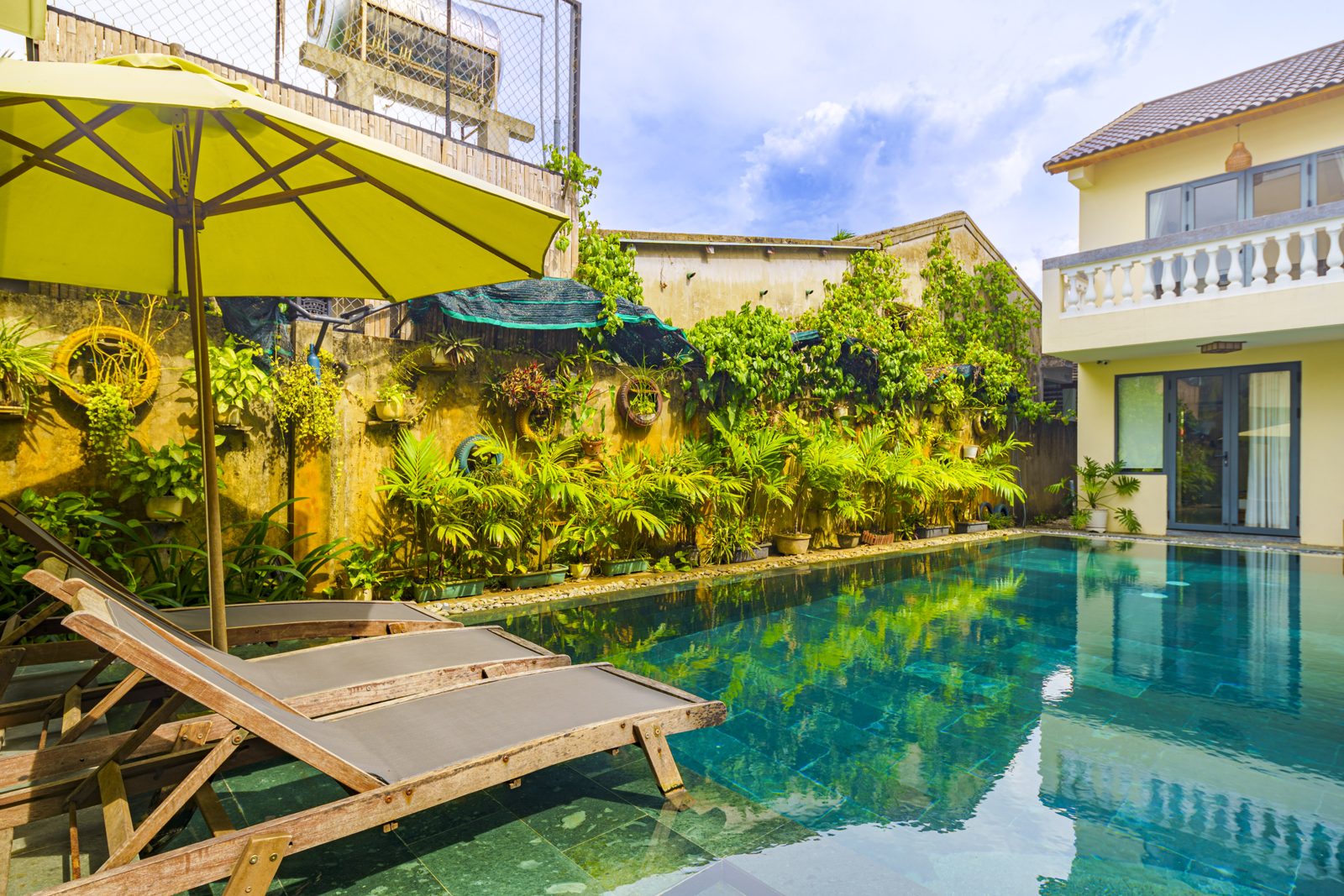 Pool with yellow umbrella, wooden loungers and garden