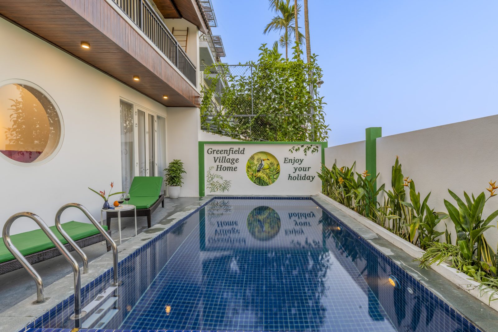 Blue-tiled pool beside the house with a round window and garden wall