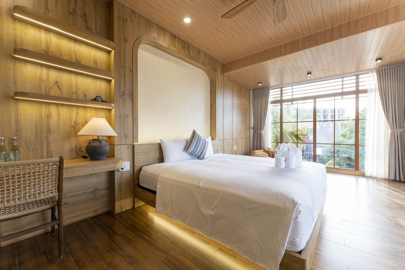 Bedroom with lit wooden shelves, desk and a big window