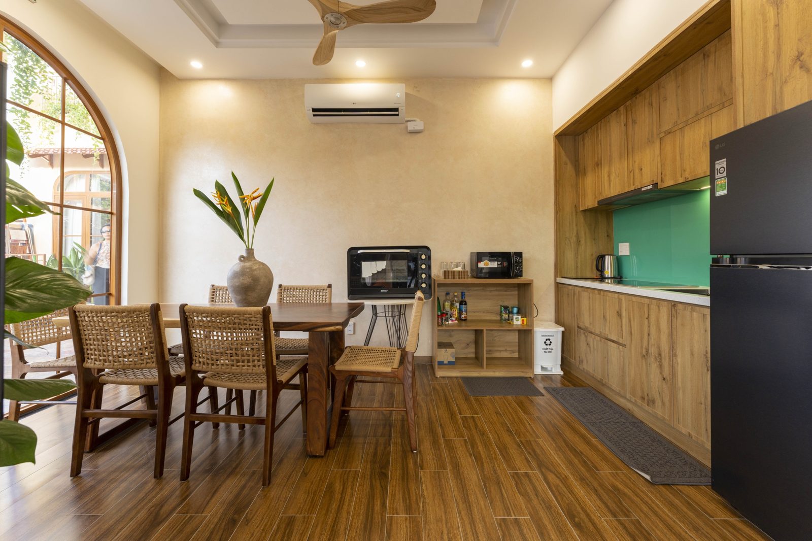 Kitchen with oak cabinets, green splashback and a wood dining table by an arched window