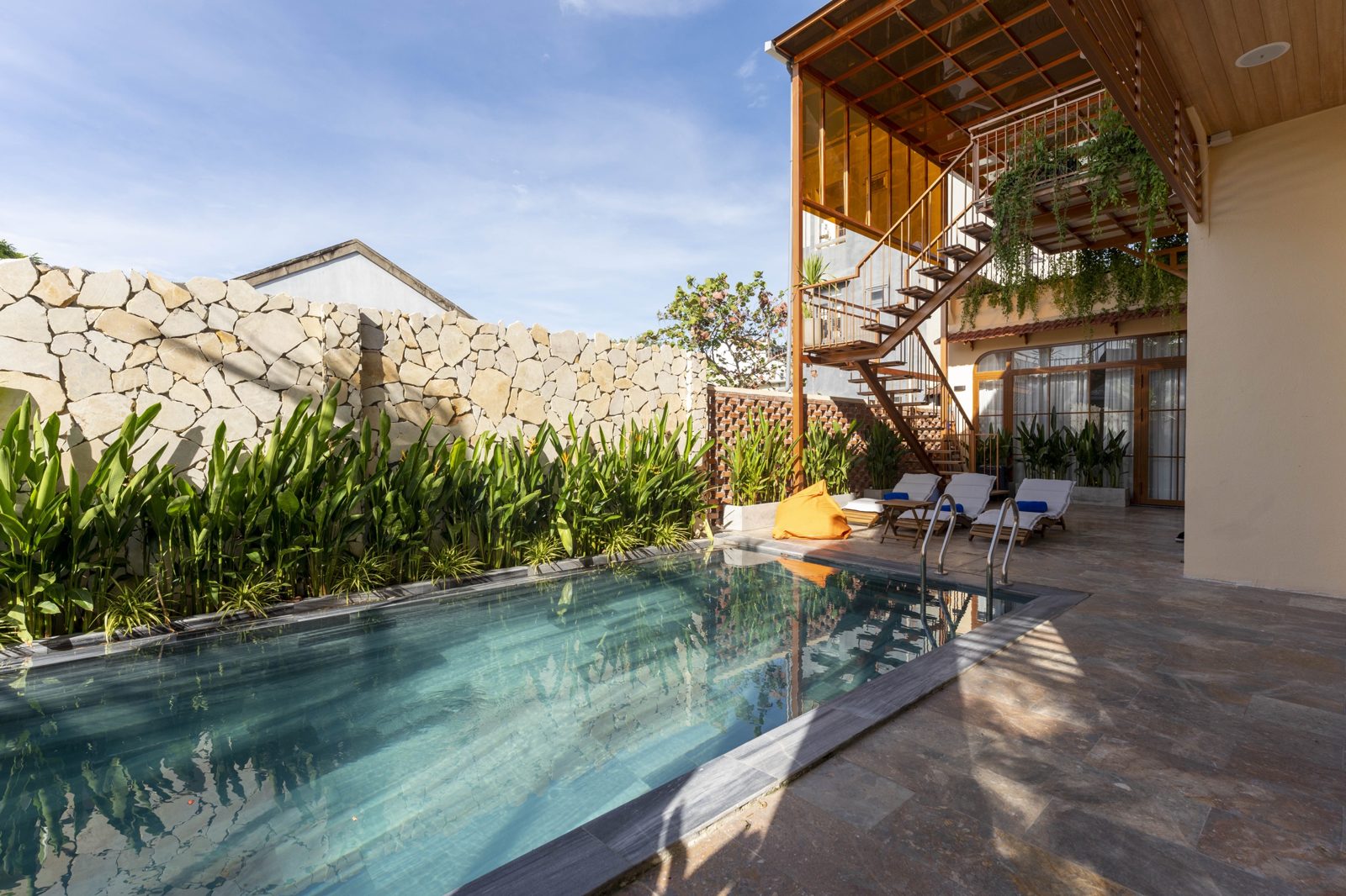 Pool beside a stone wall with an open timber staircase and hanging vines