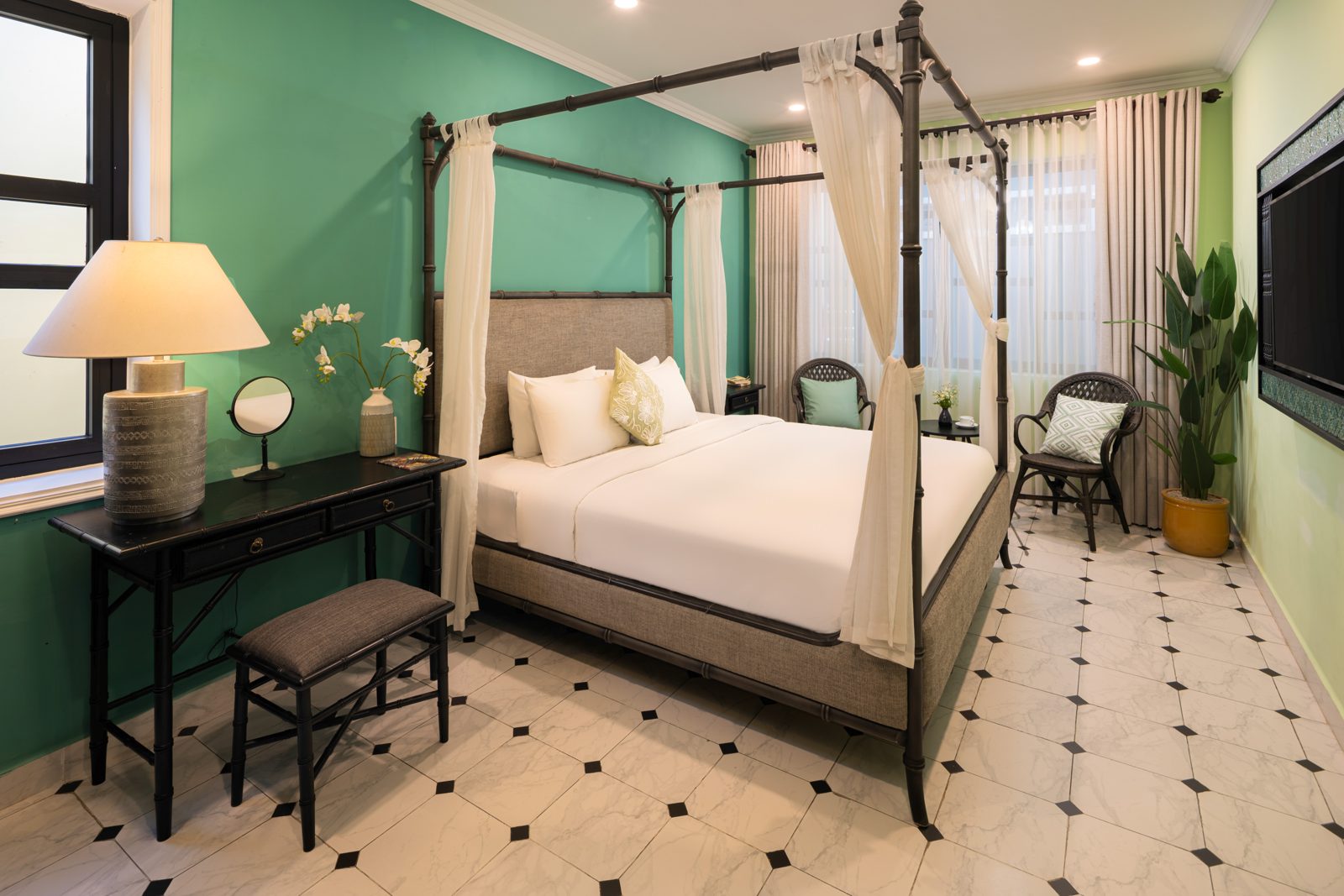Green bedroom with a black four-poster bed and linen drapes