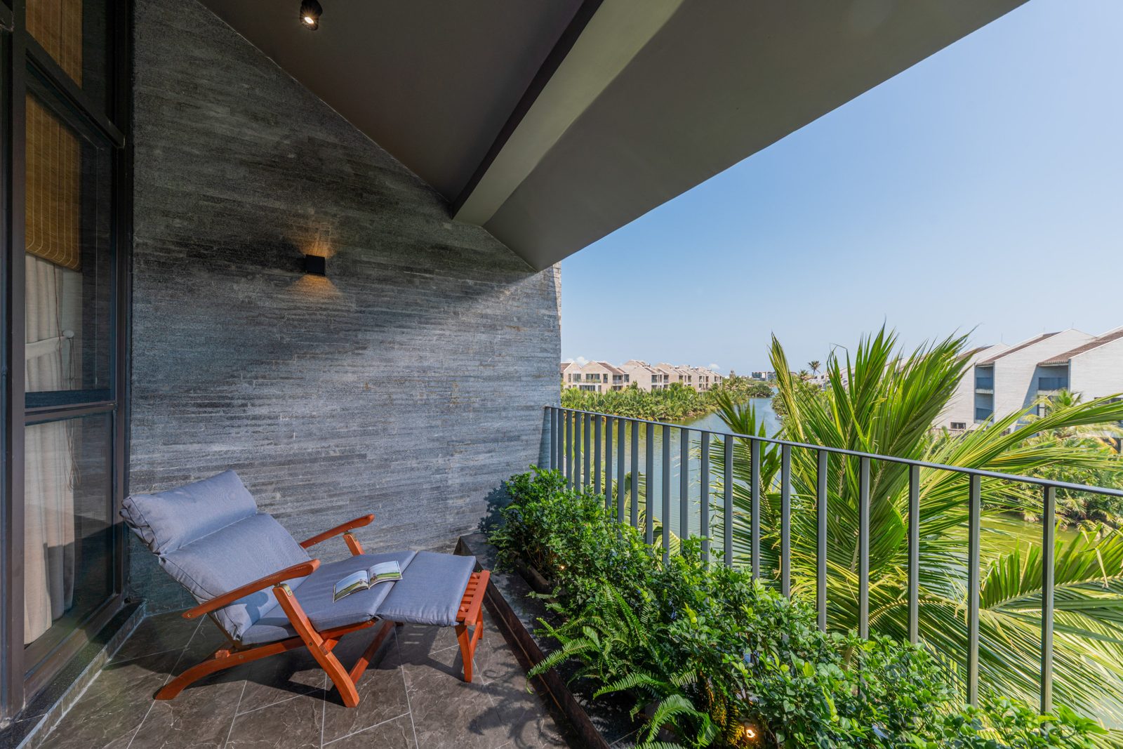 Balcony with a lounge chair beside a stone wall and palms