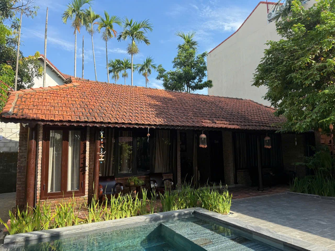 Red-tiled brick house with a veranda beside the pool and palm trees