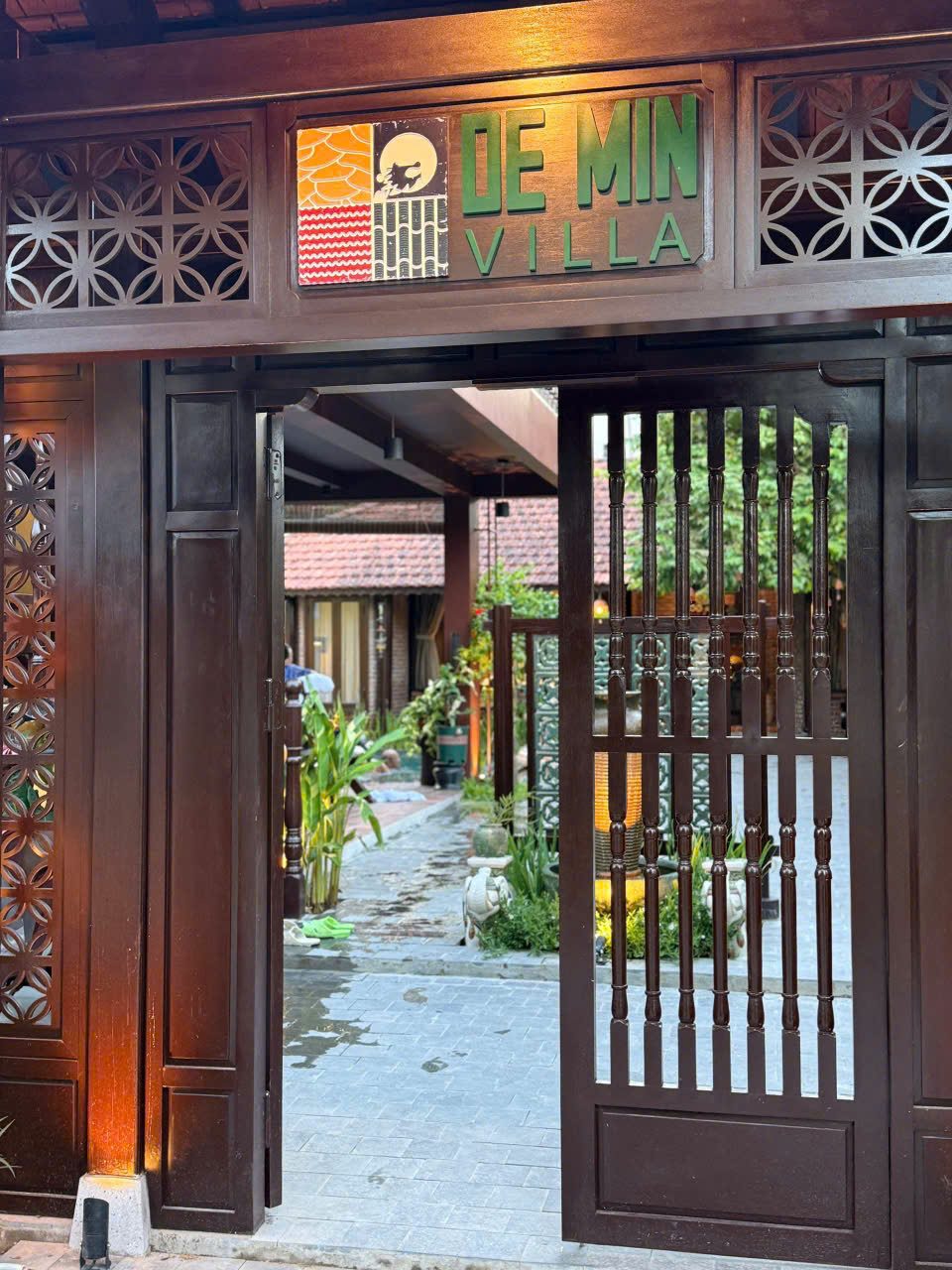 Carved wooden gate under a De Min sign, opening onto the garden