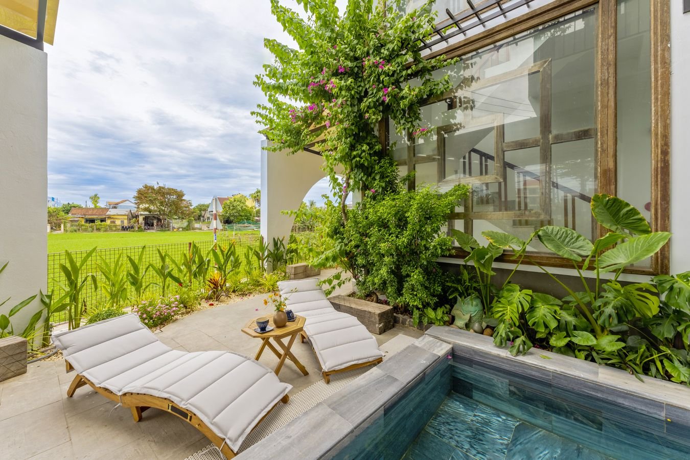 Pool corner with loungers, tropical planting and rice fields beyond