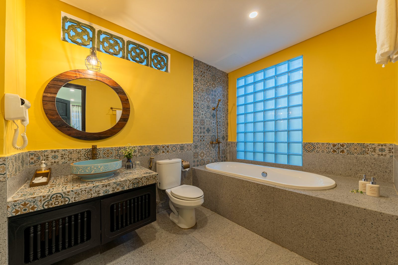 Yellow bathroom with a freestanding tub, glass-brick window and mosaic tiles